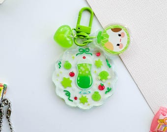 May include: Green and white keychain with a green drink, a turtle, and a star design. The keychain also features a green heart charm and a cartoon character with a green and white striped shirt.
