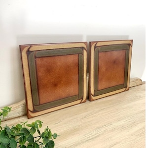 May include: Two square ceramic tiles featuring a central reddish-brown field surrounded by a dark olive green border and an outer cream-colored frame. The tiles have a smooth, glazed finish with subtle color variations across the surface.