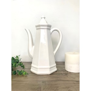 May include: A set of three ceramic mugs with a speckled, matte finish. The mugs are in shades of cream, light gray, and dark gray. Each mug has a simple, minimalist design and a rounded handle.