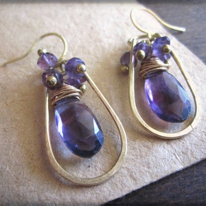 Puede incluir: Un par de pendientes de oro con una piedra preciosa de amatista en forma de lágrima y cuentas de amatista más pequeñas. Los pendientes están hechos con alambre envuelto alrededor de las piedras preciosas.
