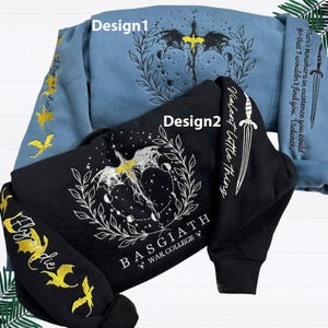 Puede incluir: Dos sudaderas, una azul claro y otra negra, con diseños bordados. La sudadera azul claro presenta un diseño de dragón y luna, con texto en la manga y la espalda. La sudadera negra tiene un diseño de dragón similar y texto.