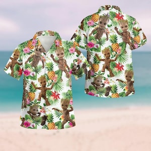 May include: White short-sleeved button-up shirt with a tropical print featuring a cartoon character. The print includes pineapples, flowers, and green leaves.