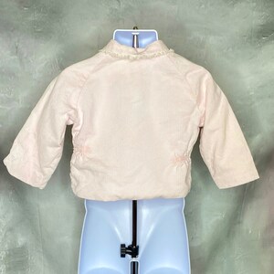 May include: A pink corduroy jacket with a white lace trim around the collar. The jacket has a zipper closure and long sleeves.
