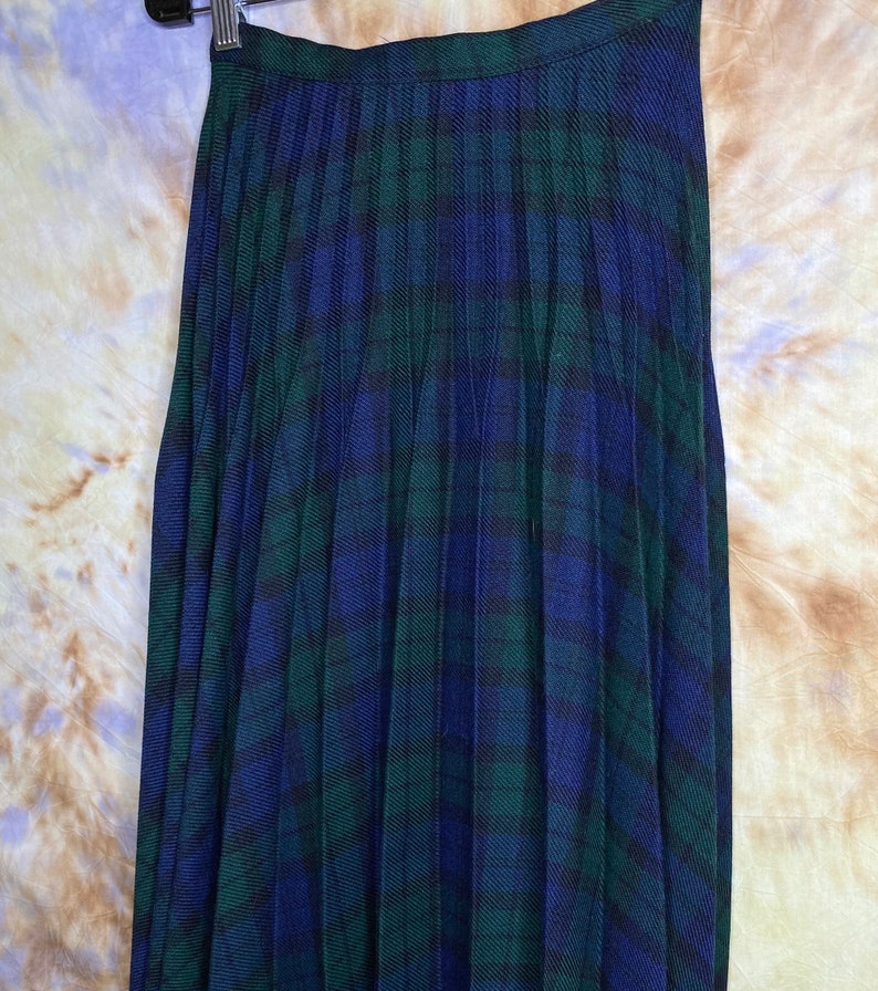 May include: A pleated skirt in a blue and green tartan pattern. The skirt is made of a soft, flowing fabric and has a classic, timeless style.