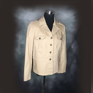 Könnte beinhalten: Eine beige Utility-Jacke mit doppelreihigem Verschluss und zwei Pattentaschen. Die Jacke hat einen Kragen und lange Ärmel.