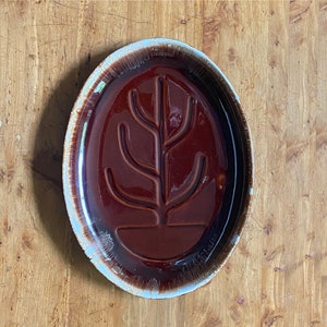 May include: A brown and blue oval ceramic serving platter with a tree-like design in the center.