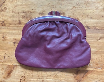 May include: A burgundy leather coin purse with a gold clasp and a smooth, slightly textured surface.