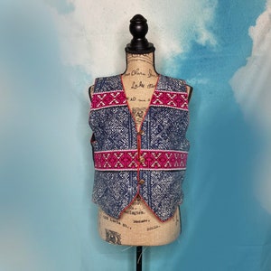 Puede incluir: Un chaleco azul y rosa con estampado y cierre de botón. El chaleco tiene un diseño geométrico con detalles en blanco y rosa.
