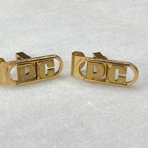 Puede incluir: Un par de gemelos de oro con las letras "PC" grabadas.