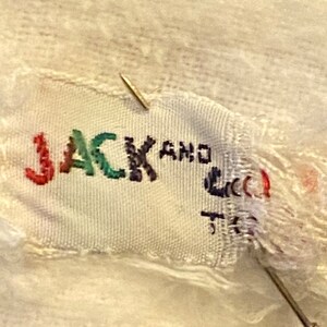 May include: A white fabric label with the text "JACK AND" in colorful embroidery. The label is torn and frayed around the edges.