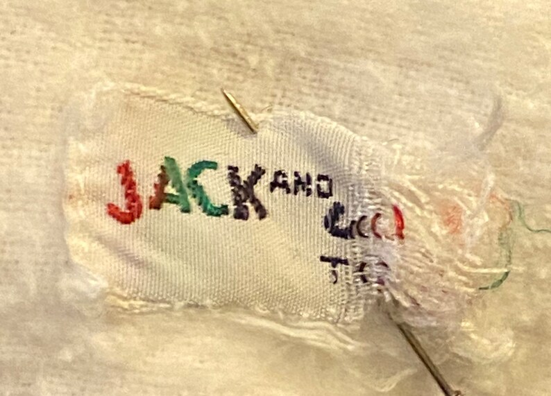 May include: A white fabric label with the text "JACK AND" in colorful embroidery. The label is torn and frayed around the edges.
