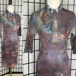 Puede incluir: Un vestido de estilo vintage con un estampado tie-dye en tonos azules, morados y rosas. El vestido tiene cuello y cierre de botón.