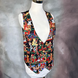 May include: A black vest with a colorful Christmas-themed pattern featuring teddy bears, wrapped gifts, and festive decorations. The vest is displayed on a mannequin with a white base and gold-colored top.