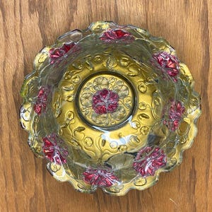 May include: A vintage glass bowl with a scalloped edge and a floral design. The bowl is clear glass with a gold iridescent finish and red flowers.
