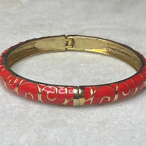 May include: A gold bangle bracelet with a red enamel design featuring swirling patterns.