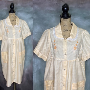 May include: A yellow and white gingham button-up dress with short sleeves and embroidered flowers. The dress has a white lace trim around the collar and pockets on the front.
