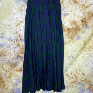 May include: A long, pleated skirt in a blue and green tartan pattern. The skirt has a waistband with a button closure.