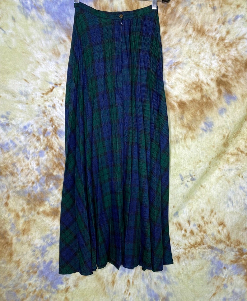 May include: A long, pleated skirt in a blue and green tartan pattern. The skirt has a waistband with a button closure.