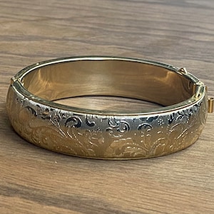 May include: A gold bangle bracelet with a floral engraved design.