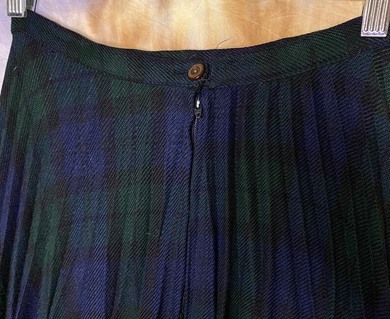 May include: A black, green and blue plaid skirt with a zip fastening. The skirt is pleated and has a waistband.