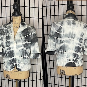 May include: A black and white tie-dye blazer with a zipper closure and short sleeves. The blazer has a pocket on the front.