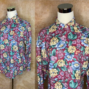 May include: A long-sleeved button-up shirt with a floral print in shades of pink, blue, yellow, and green on a burgundy background.