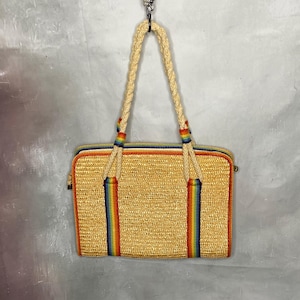 May include: A rectangular straw handbag with a woven texture, featuring a rainbow stripe design and rope handles. The bag has a zipper closure and is trimmed with orange and blue accents. The handles are attached with rainbow-colored accents.