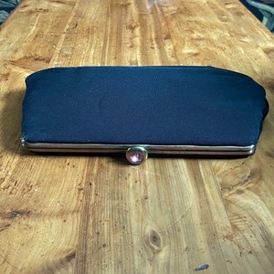 May include: A black fabric clutch purse with a gold metal frame and a pink rhinestone clasp.