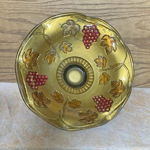 May include: A gold glass bowl with a scalloped edge and a grapevine design. The bowl is decorated with red and gold grapes and leaves.