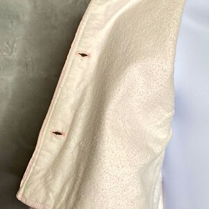 May include: A white corduroy jacket with a pink lining and two black buttons. The jacket is folded in half and the lining is visible.