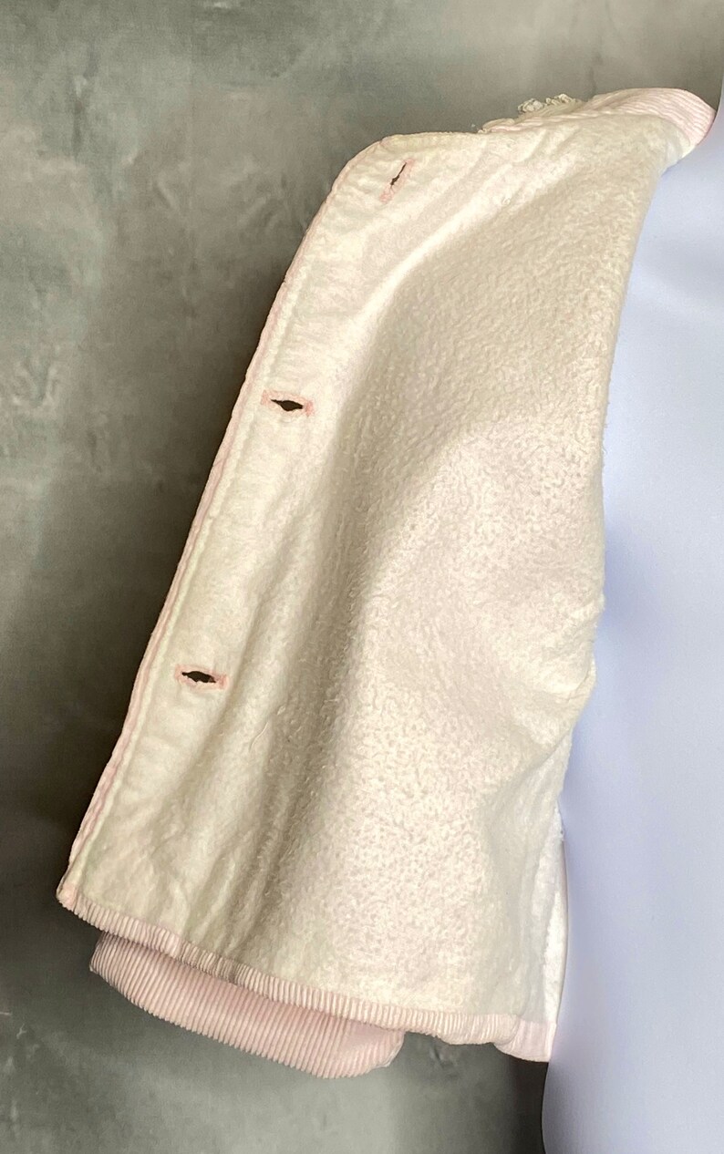 May include: A white corduroy jacket with a pink lining and two black buttons. The jacket is folded in half and the lining is visible.