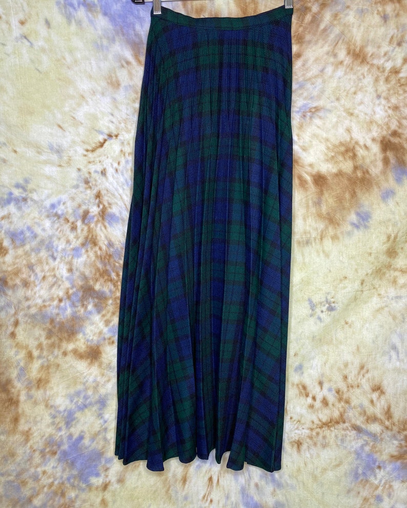 May include: A long, pleated skirt in a blue and green tartan pattern. The skirt has a waistband and is made of a soft, flowing fabric.