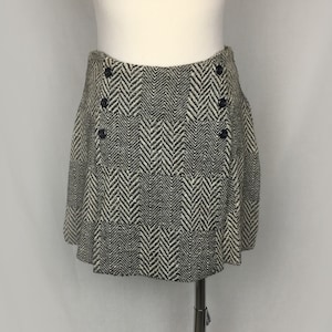 May include: A black and white herringbone patterned skirt with a button closure. The skirt is pleated and has a short length.
