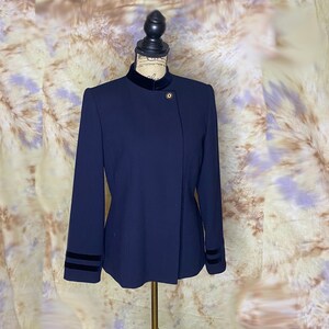 May include: A navy blue blazer with a mandarin collar and velvet trim on the collar and cuffs. The blazer has a single gold button closure.