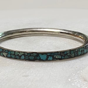 May include: A silver bangle bracelet with a turquoise inlay. The turquoise is set in a mosaic pattern around the entire bracelet.