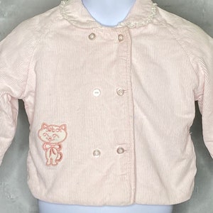 May include: A pink corduroy jacket with a white lace collar and a pink embroidered cat on the front.