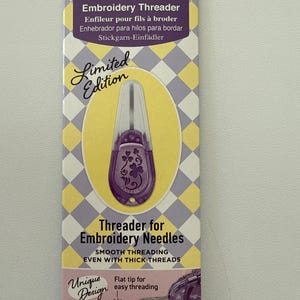 May include: A purple and clear embroidery threader on a patterned card. The card has text in multiple languages, including "Embroidery Threader" and "Limited Edition." The threader is designed for embroidery needles and features a flat tip for easy threading.