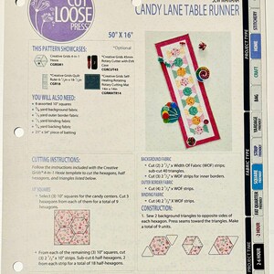 May include: A sewing pattern for a Candy Lane Table Runner, featuring a pink, green, and blue patchwork design. The pattern includes instructions for cutting and constructing the runner, which measures 50 inches by 16 inches. The pattern also includes a list of materials needed, including fabric, batting, and rotary cutting tools.
