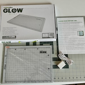 May include: A white and gray LED light board with a grid pattern and the text "GLOW MINI" on the box. The light board is used for crafts, quilting, and sewing. It has adjustable illumination and a non-slip self-healing cutting mat.