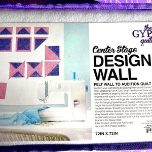 May include: A white felt design wall kit with a purple border, featuring a sewing machine and quilt block designs. The text reads "Center Stage DESIGN WALL" and measures 72in x 72in.