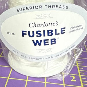 May include: A spool of white Charlotte's Fusible Web thread, 100% nylon, in a clear plastic wrapper. The label reads "Superior Threads" and "TEX 70". The text "Not for use on a longarm" and "Not for use as a top thread" are also visible.