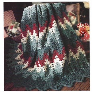 May include: A crocheted blanket featuring a chevron pattern in alternating stripes of dark green, deep red, and cream. The textile has a textured, open-work stitch design with a scalloped edge, showcasing a repeating zigzag motif throughout the fabric.