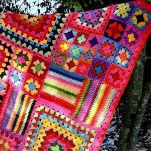 May include: A handmade crochet blanket featuring a vibrant patchwork of multi-coloured granny squares and rectangular striped sections. The textile displays a wide array of bright hues including red, pink, yellow, blue, green, and purple yarn.