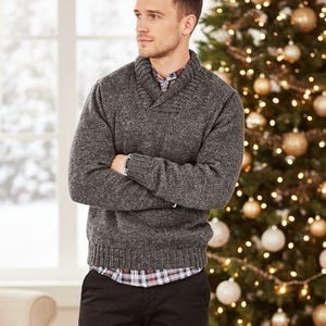 May include: A charcoal gray knit sweater with a shawl collar, worn over a plaid button-down shirt and black trousers. The sweater features a textured, heathered appearance with ribbed cuffs and a ribbed hem, providing a layered look.