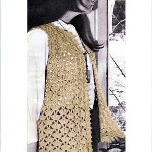 Op de afbeelding: Een mouwloos, beige gehaakt vest met een ingewikkeld, herhalend waaiervormig patroon over het hele kledingstuk. Het vest wordt gedragen over een effen wit shirt met lange mouwen en een donkere broek, met een lange hangerketting op de borst.