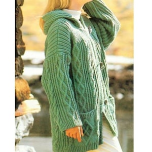 May include: A sage green hooded cardigan featuring a chunky cable knit pattern, long sleeves, and a front button closure with toggle-style fasteners. The garment includes two large patch pockets on the front and a ribbed hem and cuffs.