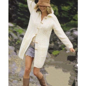 May include: A long-sleeved, off-white cable knit cardigan featuring a hood, a button-down front with light-colored toggles, and two front pockets. The garment is paired with a light blue denim mini skirt and brown knee-high boots.