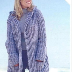 May include: A periwinkle blue, chunky knit, open-front cardigan featuring a hood, long sleeves with wide cuffs, and two large front patch pockets. The garment has a vertical ribbed texture and includes a tag stating Includes Larger Sizes.