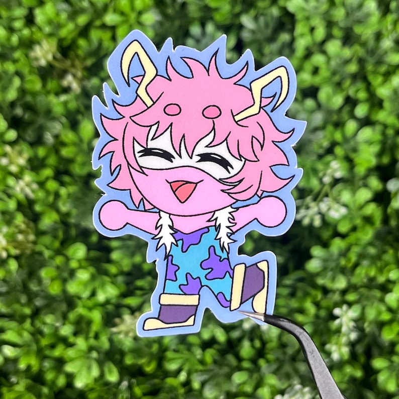 May include: A sticker featuring a cartoon character with pink hair and a light blue outline. The character is smiling and wearing a blue and purple outfit. The sticker is held by tweezers against a green background.