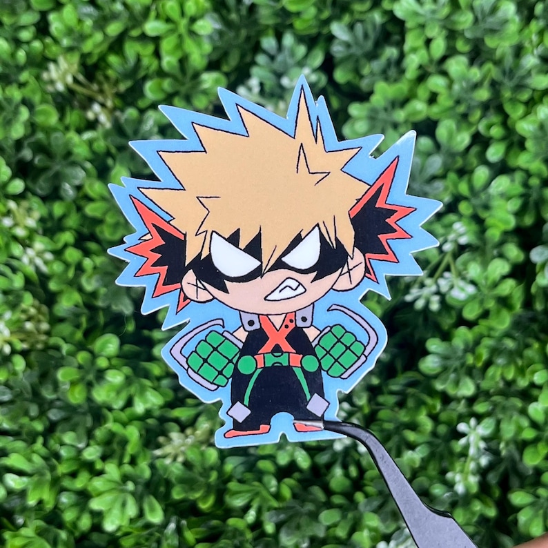 May include: A sticker featuring a cartoon character with spiky blonde hair, black eyes, and a determined expression. The character wears a black outfit with green and orange accents, set against a light blue jagged outline.